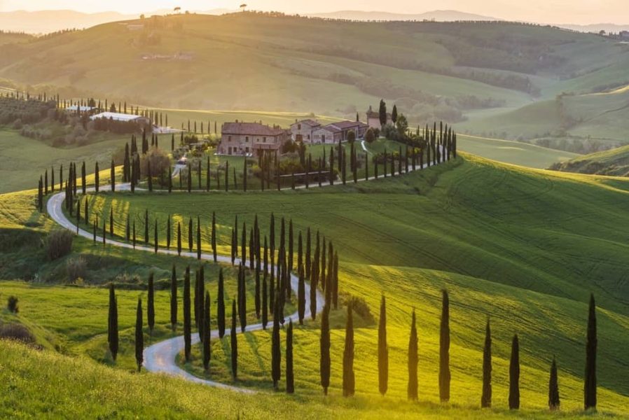 Tuscan countryside with rolling hills, lush green fields, and villas bathed in sunshine.