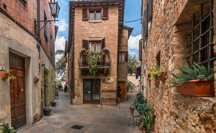 A picturesque Tuscan village with red brick buildings and charming cobblestone walkways under a clear blue sky.