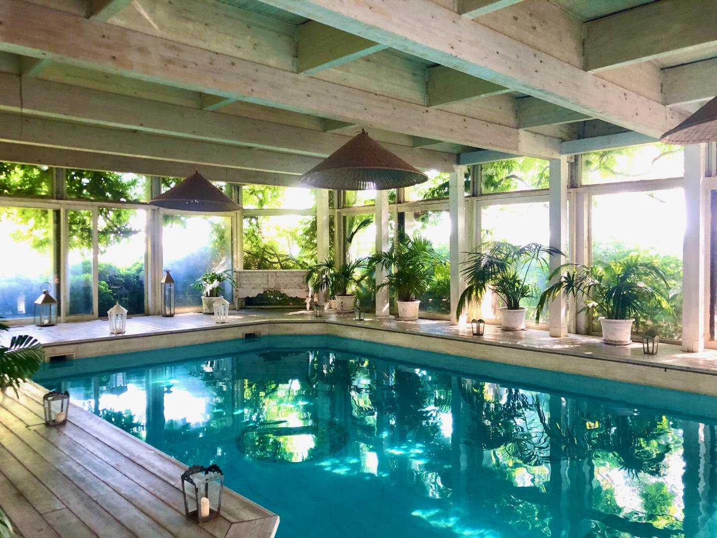 Swimming pool inside a luxury villa in Umbria, lined with plants and floor-to-ceiling windows.