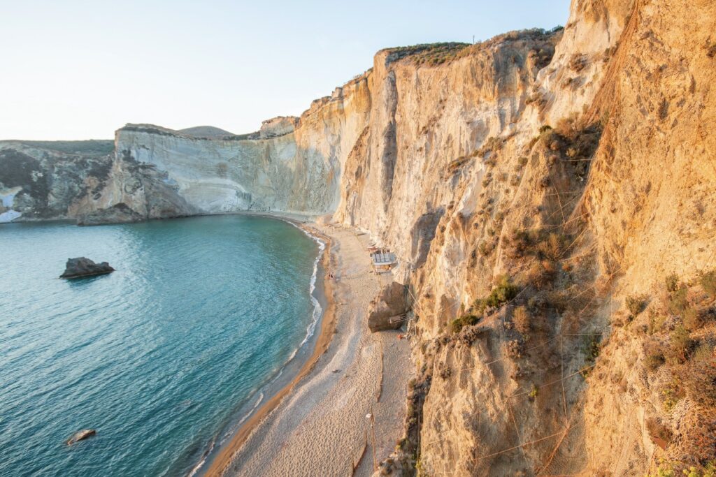Sandstone cliffs and teal blue water with a sandy beach.