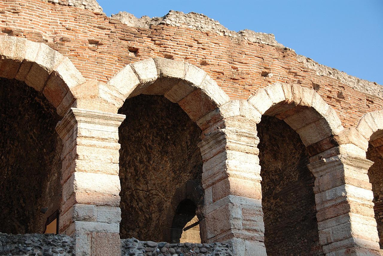 Close-up view of ancient brick and stone arches in a weathered historical structure under a clear blue sky.