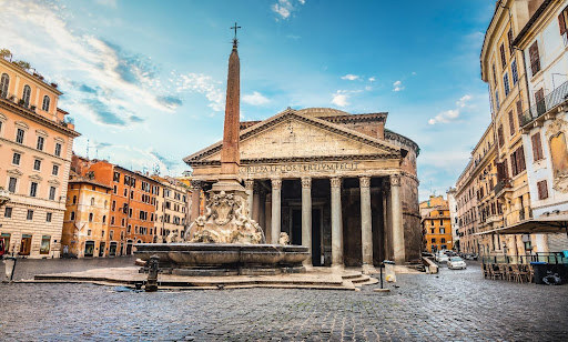 The Pantheon in Rome on a quiet winter morning, with its massive stone columns, central fountain, and surrounding historic buildings, set against a clear blue sky and nearly empty cobblestone piazza.