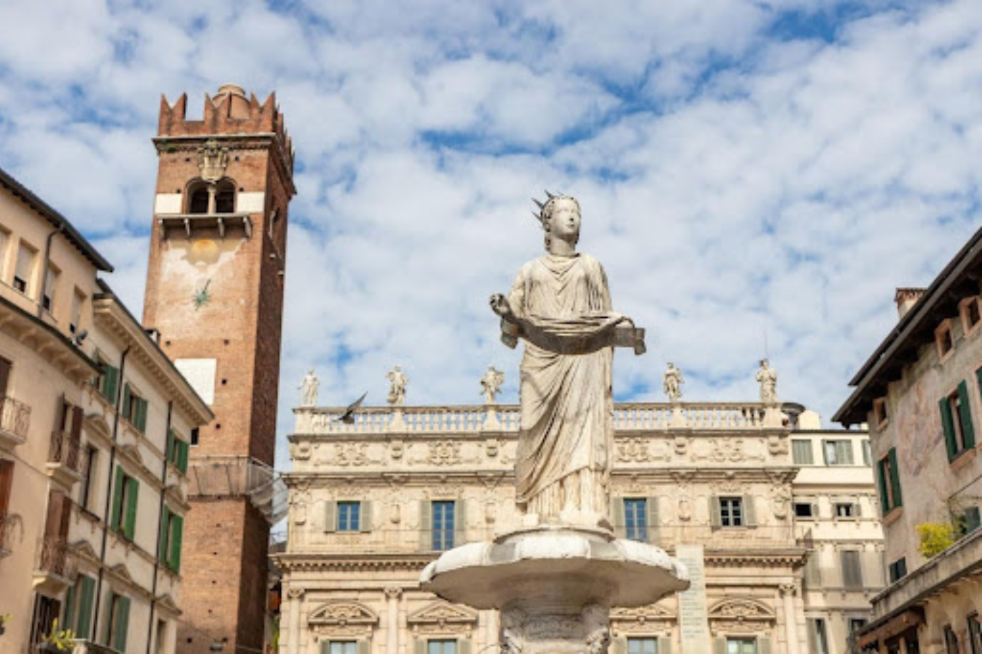 Statue in Piazza delle Erbe with historic buildings and a medieval tower in Verona, Italy under a partly cloudy sky.