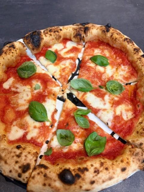 A freshly sliced Neapolitan margherita pizza with a puffy, wood-fired crust, rich tomato sauce, melted fior di latte mozzarella, and fresh basil leaves, served on a metal pizza pan — the best pizza in Rome.