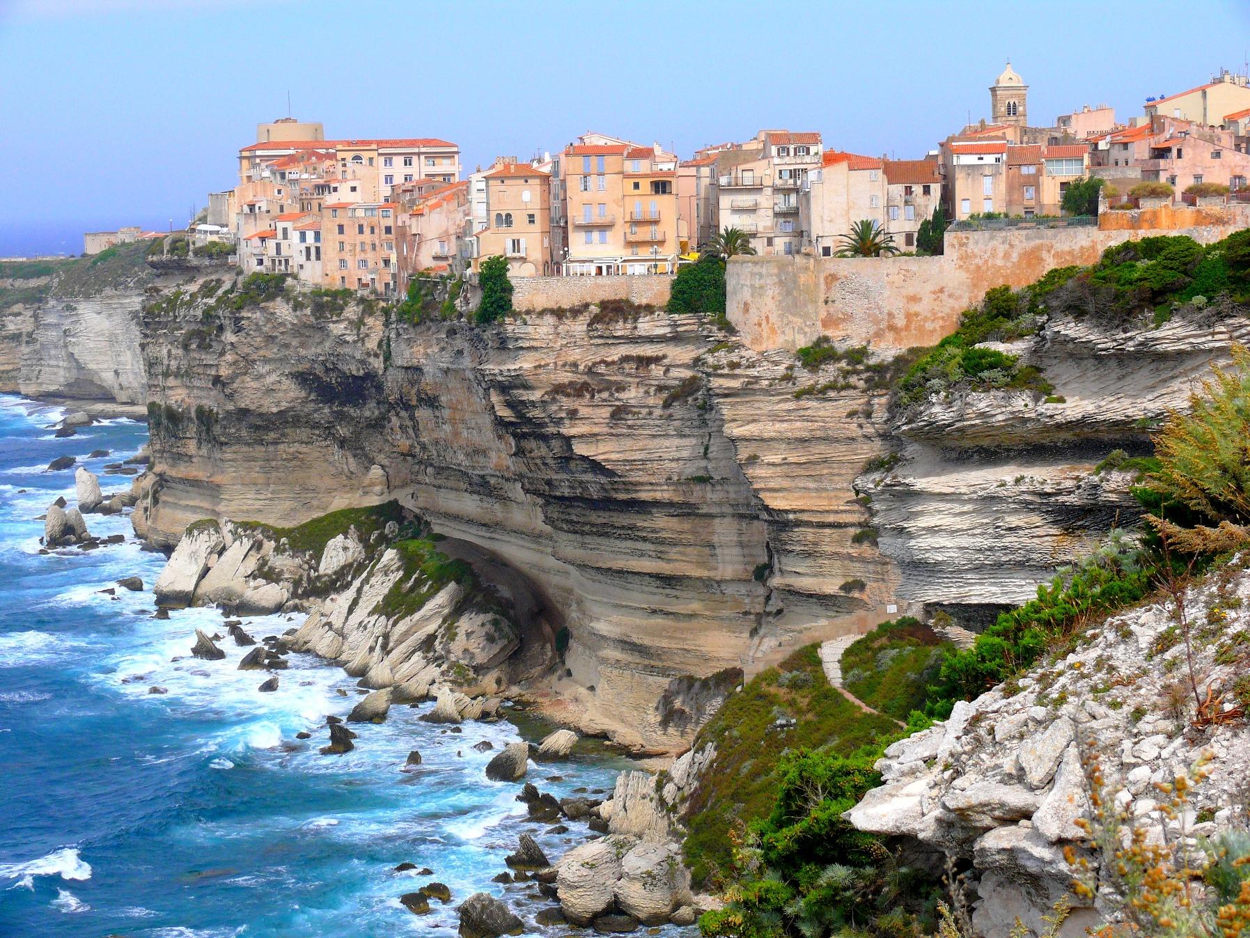 Cliffs on the northern coast of Sardinia with orange buildings on top and water below.
